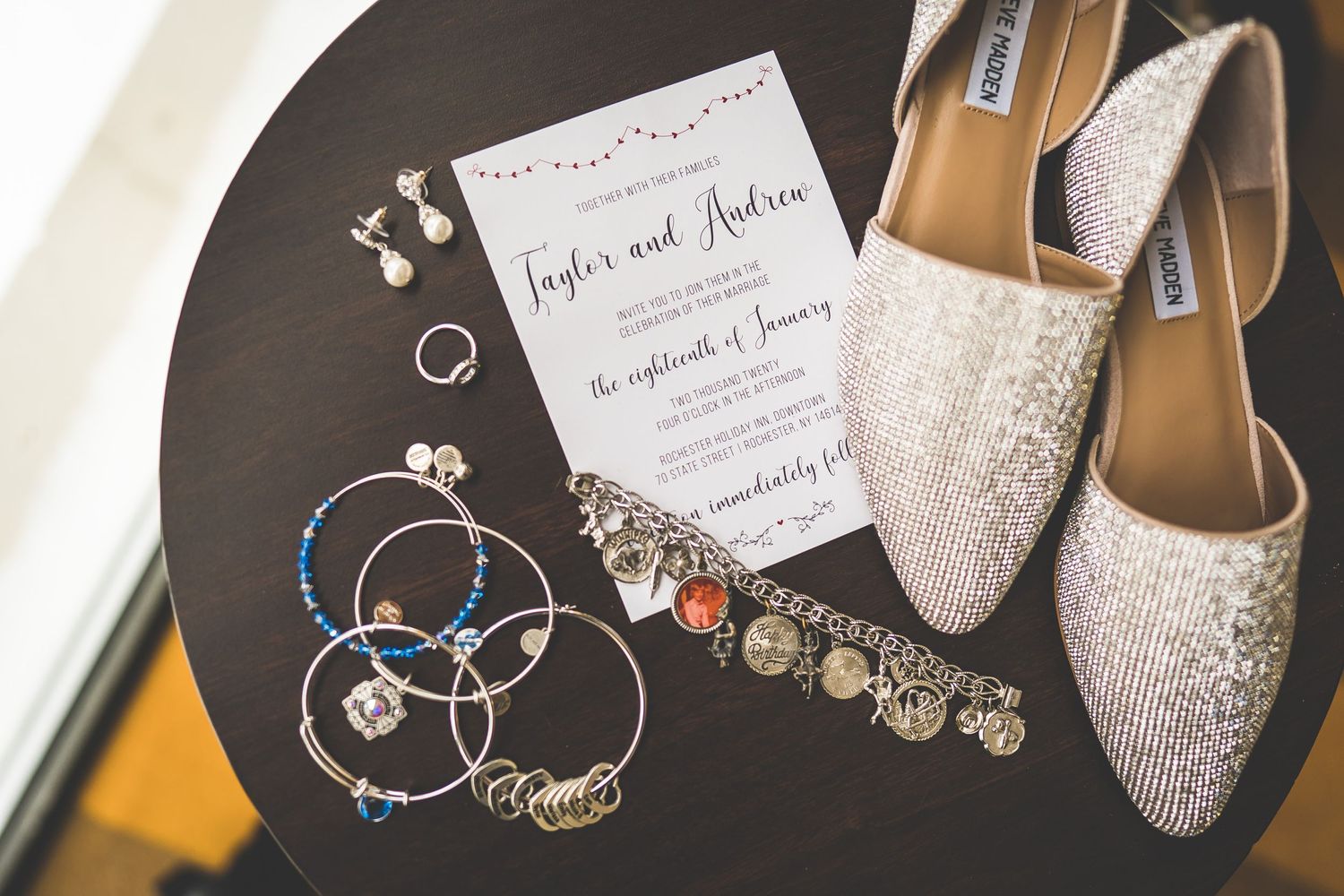 Wedding accessories including sparkly shoes and invitation cards arranged on dark surface.