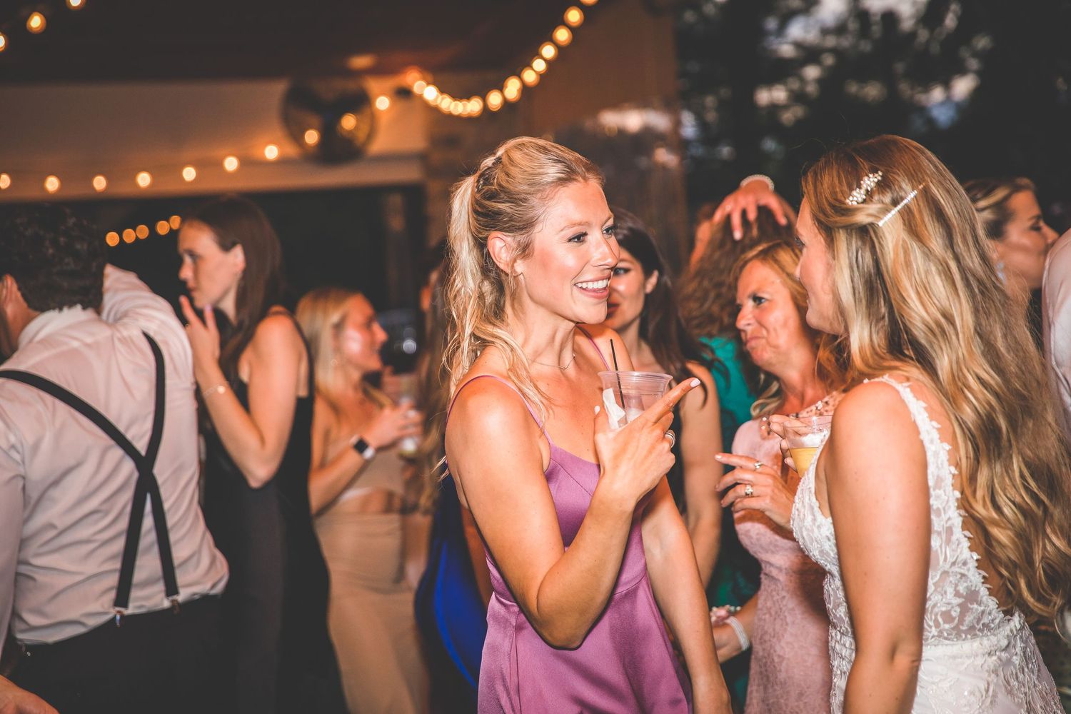 Wedding guests enjoying the dance floor under warm string lights at evening reception.