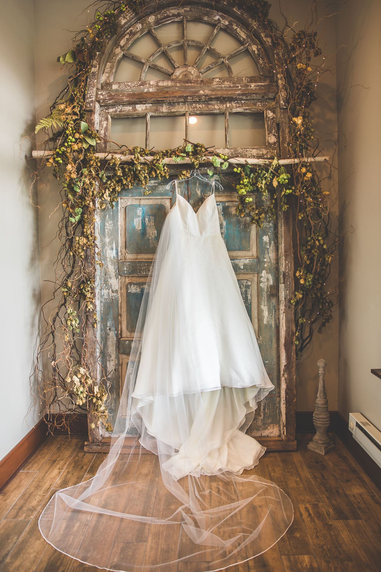 White wedding dresses displayed under a rustic wooden arch decorated with greenery and flowers.