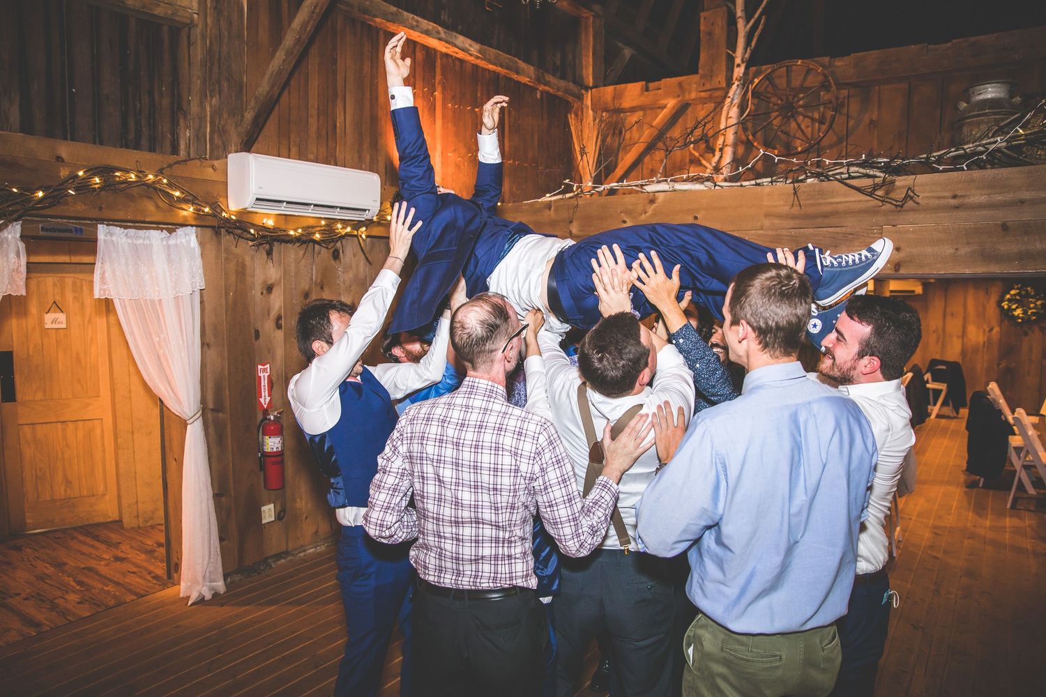 Wedding guests dancing and celebrating in a rustic barn venue at night.