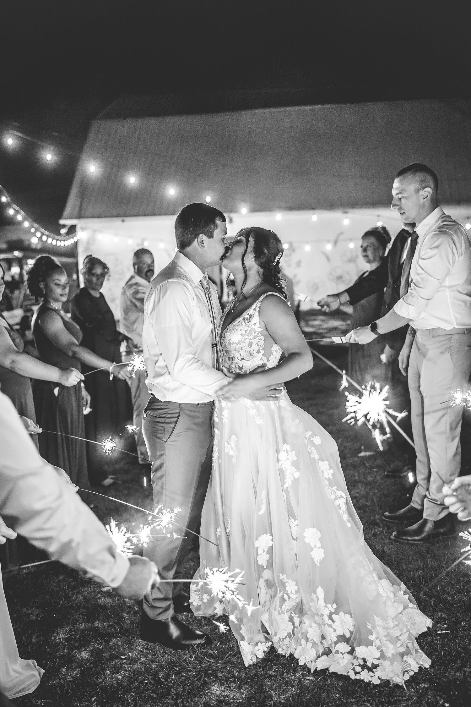 Wedding party creates a sparkler send-off tunnel in black and white photography.