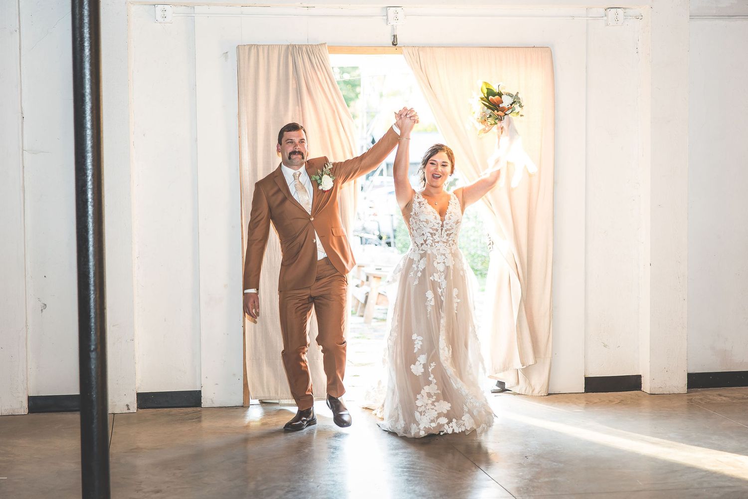 Wedding couple makes grand entrance through bright white doorway at reception venue.