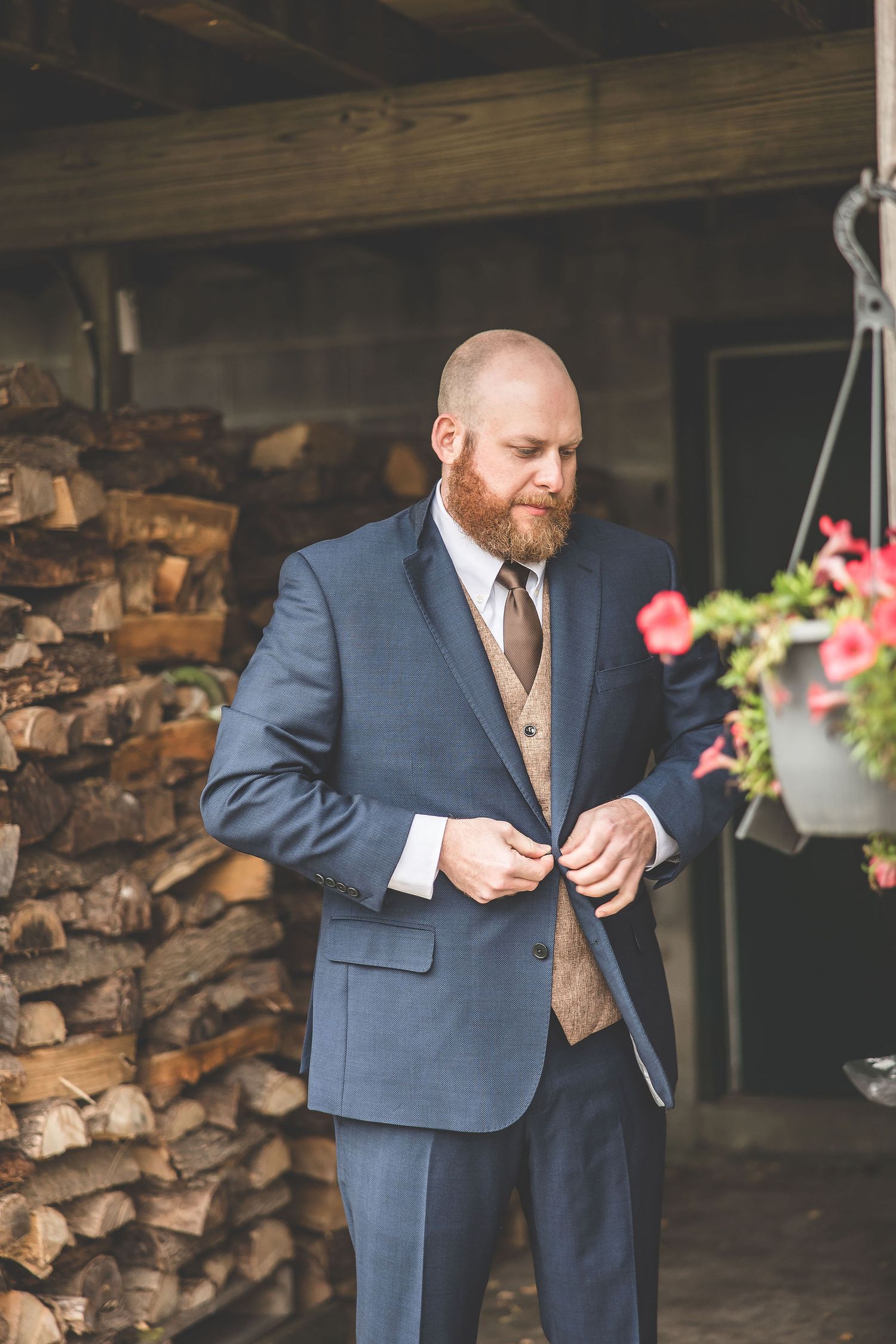 A groom in a navy suit adjusts his cuffs against a rustic wood wall background.