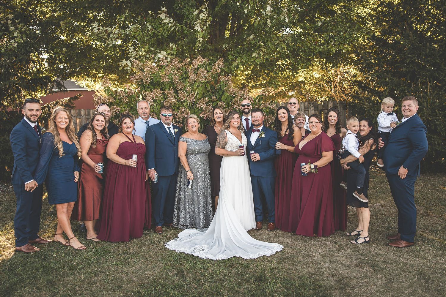 Wedding party gathered outdoors for group photos in natural autumn setting.