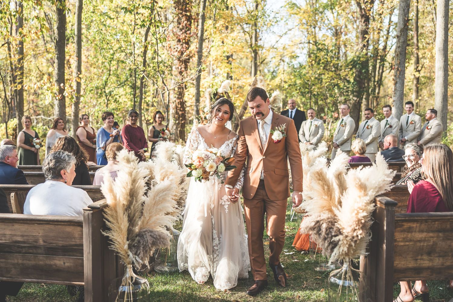 Wedding guests gathered outdoors for ceremony seating surrounded by fall foliage.