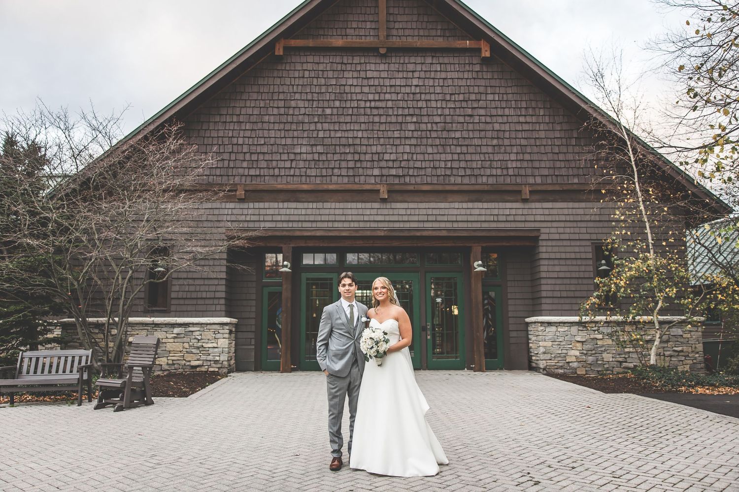 Wedding couple posing outside a craftsman-style building with stone and shingle siding.