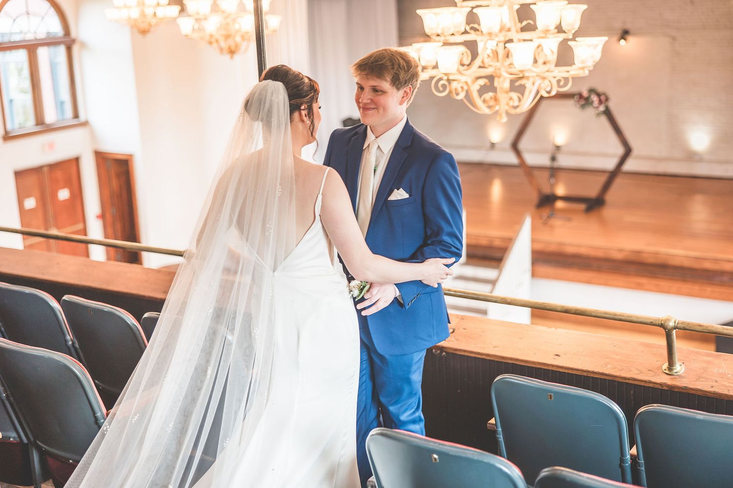 Two people share a first look moment in a wedding venue with chandeliers.