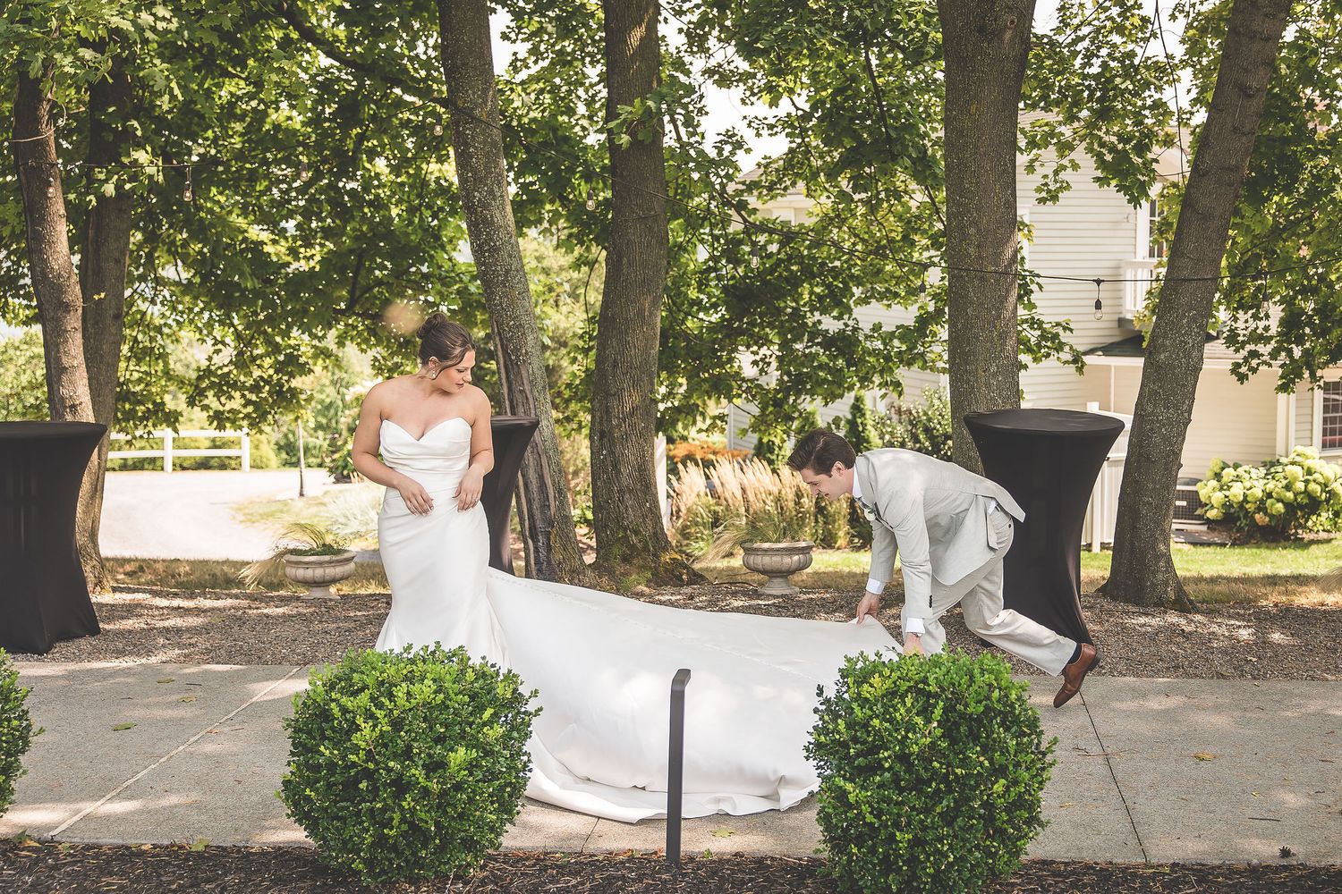Wedding couple dancing and embracing on a tree-lined pathway with manicured shrubs.