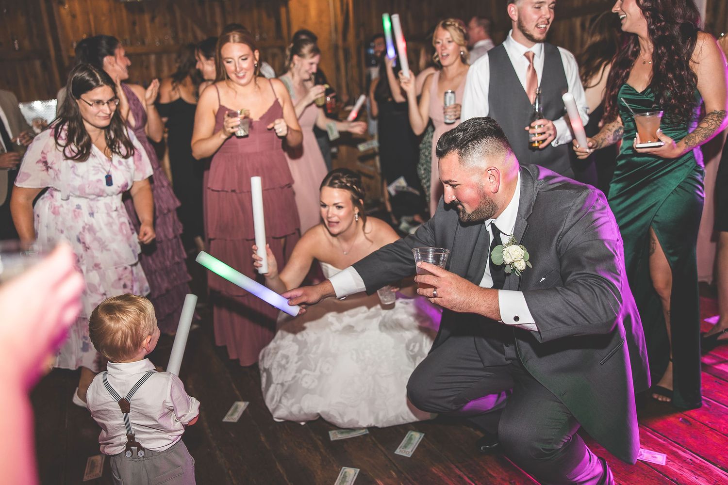 Wedding party dancing on wooden floor with purple lighting and young ring bearer.