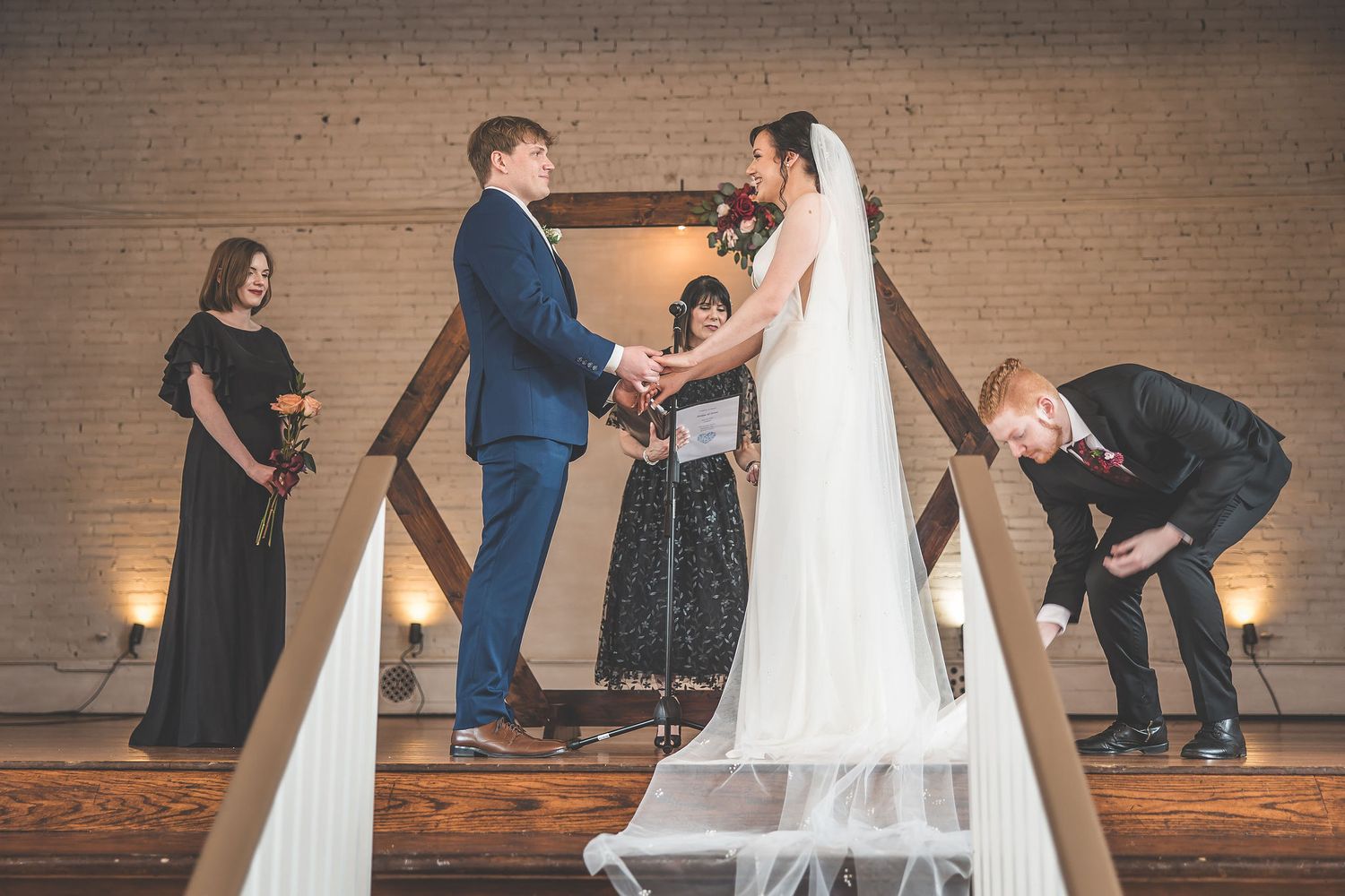 Wedding ceremony processional on a rustic wooden stage with exposed brick backdrop.