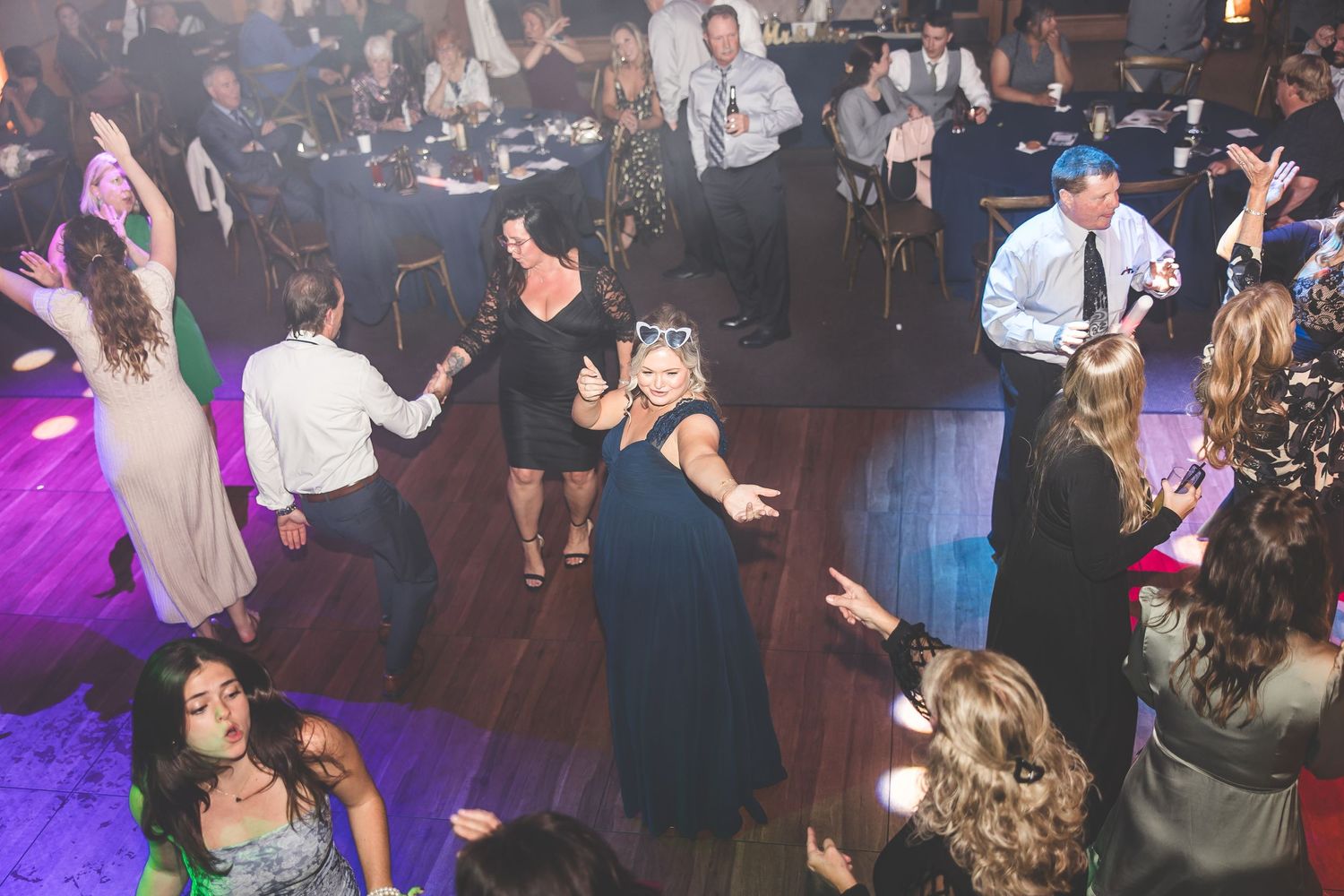 Wedding reception dance floor filled with guests celebrating under colorful lighting effects.