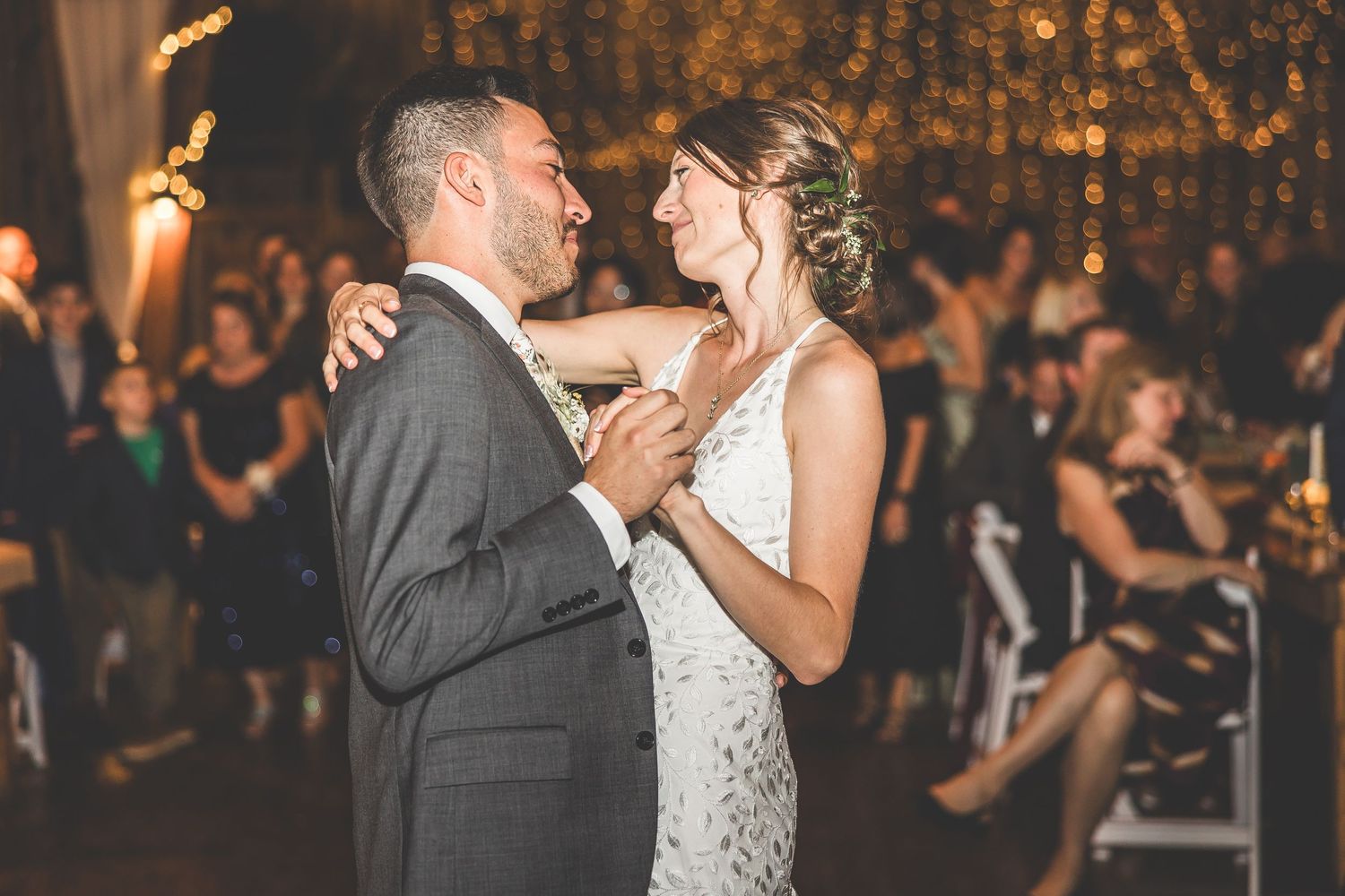 Couple shares first dance at rustic barn wedding reception with string lights.