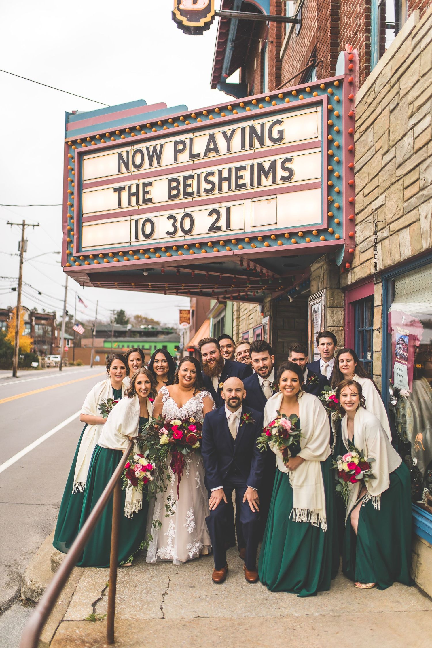 Wedding party poses outside a vintage theater marquee on a city street.