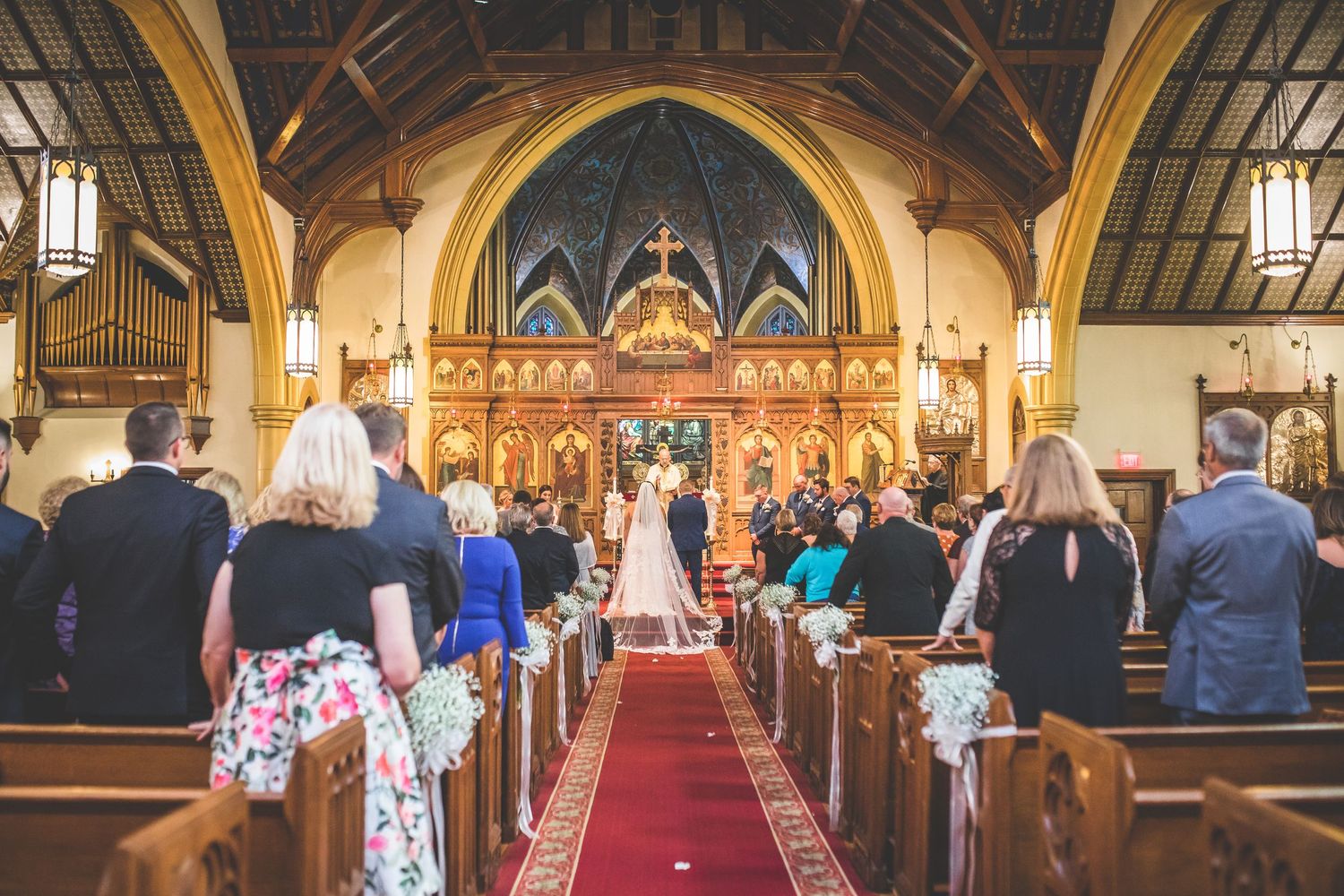 Traditional church wedding ceremony with guests seated in wooden pews and ornate stained glass windows.