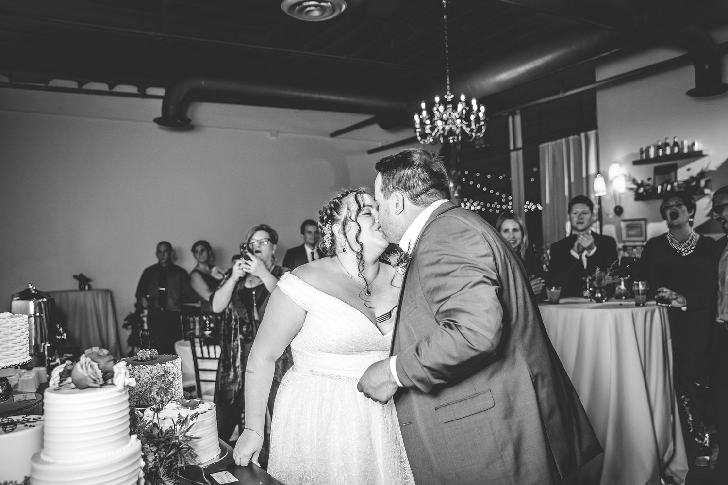 Wedding reception guests dancing and celebrating under string lights and chandeliers at an indoor venue.