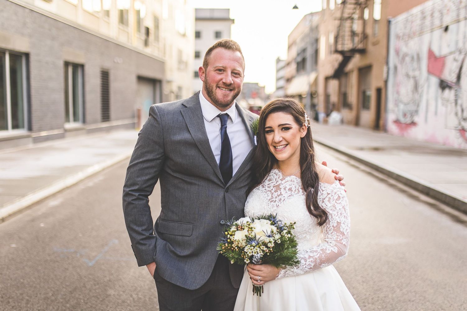 Elegant wedding party poses for portraits on city street with historic buildings.