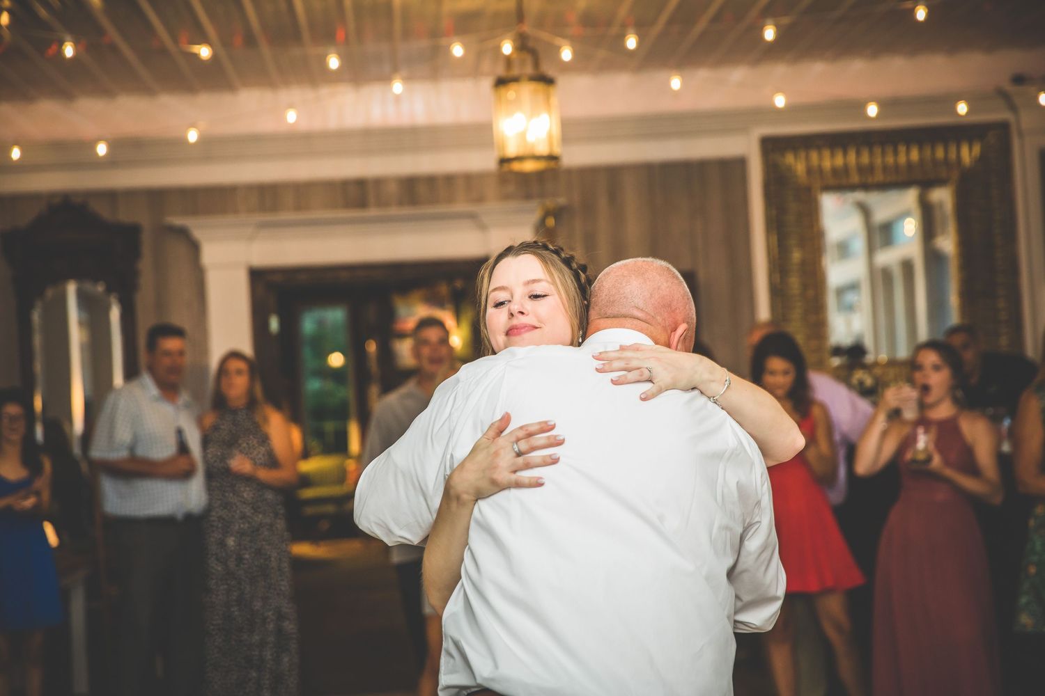 Wedding guests embrace while dancing at an indoor reception with warm lighting.