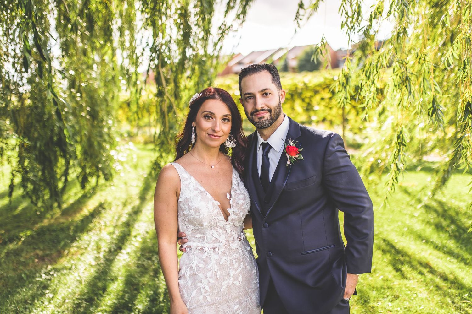 Wedding couple poses under cascading willow tree branches in a garden setting.