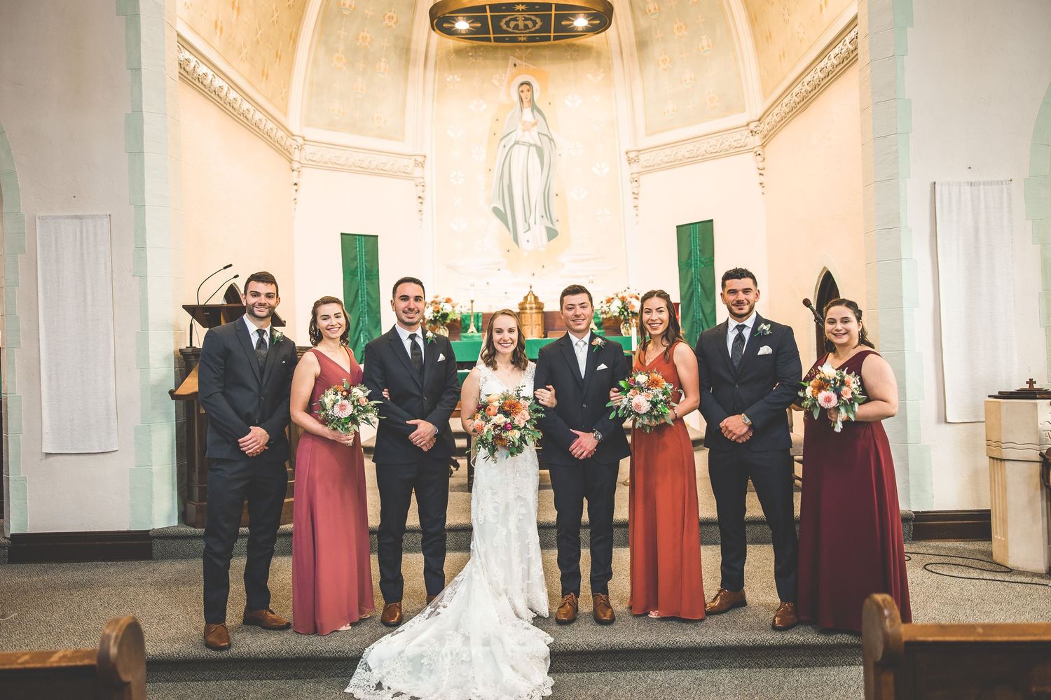 Wedding ceremony group gathered inside an elegant church with green accents and cream walls.