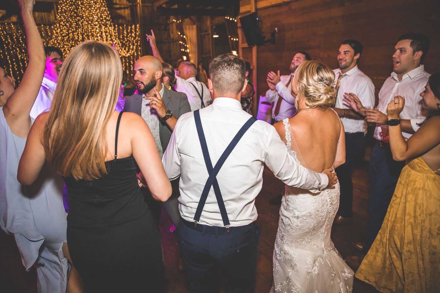 Wedding guests dancing and celebrating at a barn reception with string lights.