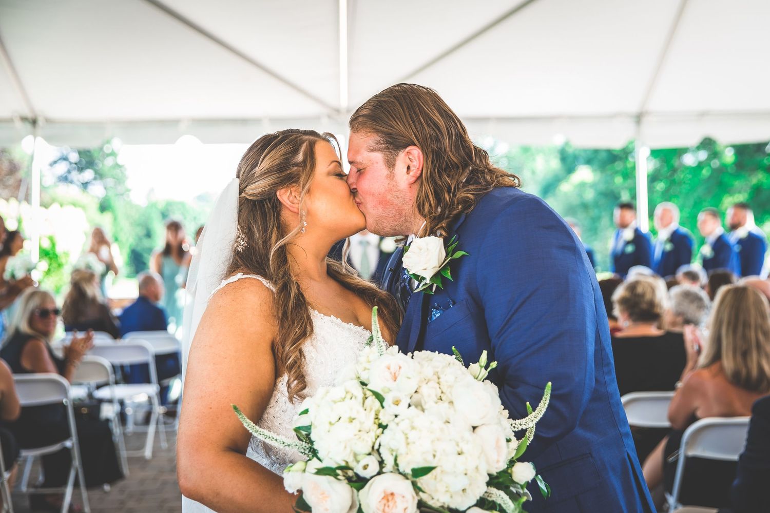 White floral bouquet being held at an elegant outdoor wedding celebration.