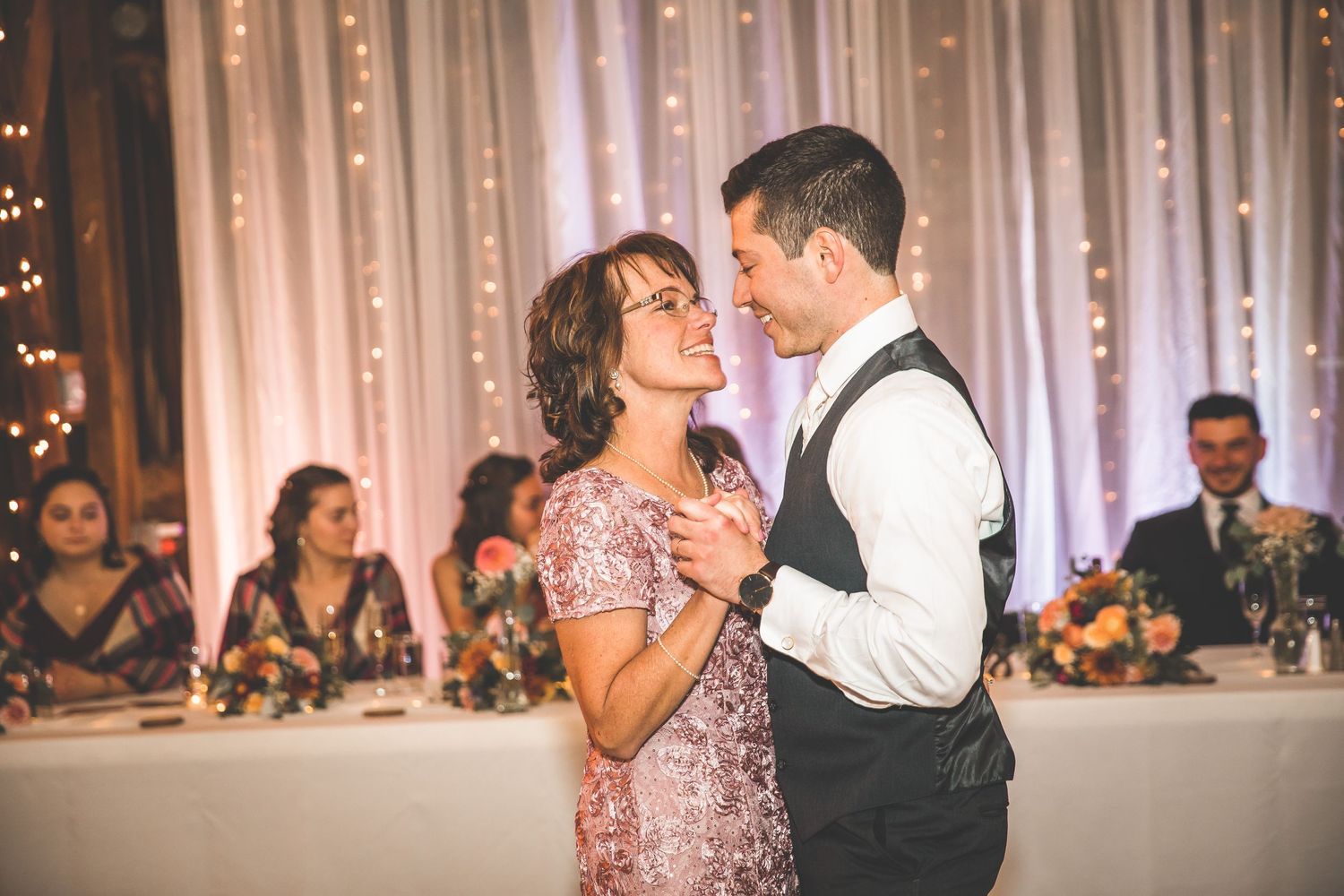 Couples dancing at an indoor wedding reception with fairy light backdrop.