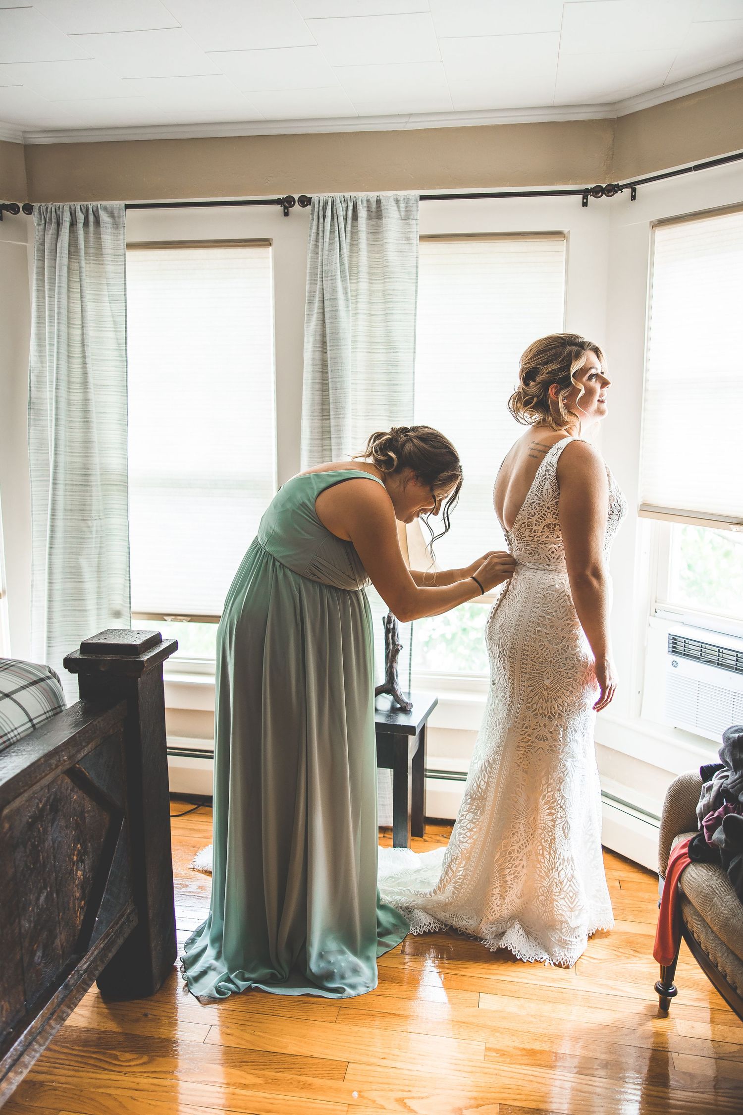 Wedding dress fitting and preparation in a sunlit room with mint green curtains.