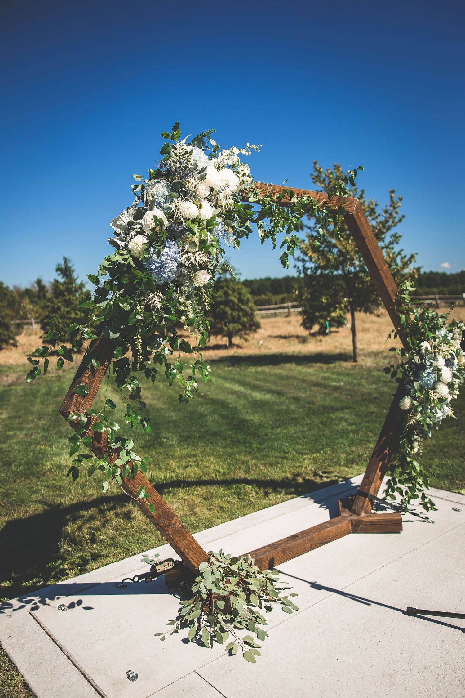 Wooden cross arch decorated with white flowers and greenery for an outdoor wedding ceremony.