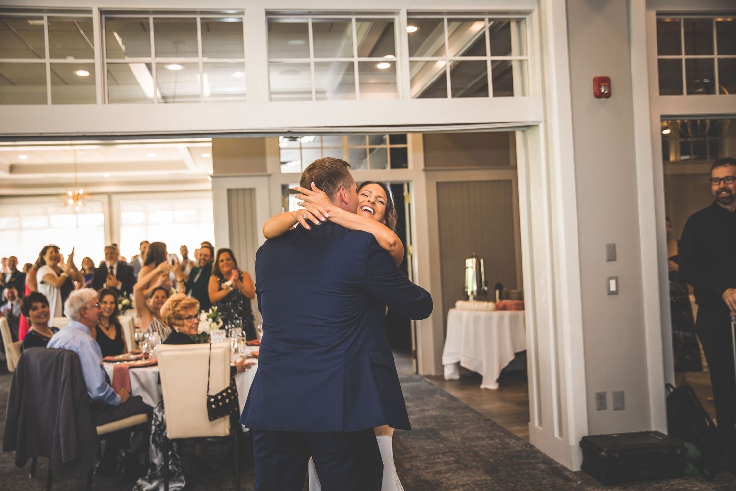 Large reception hall with white walls and windows filled with wedding guests.