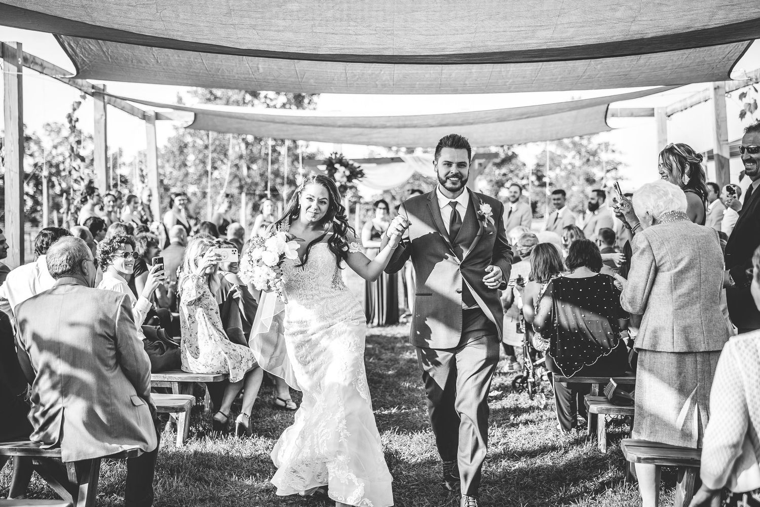 Family portrait outdoors with wedding party against rustic countryside backdrop.