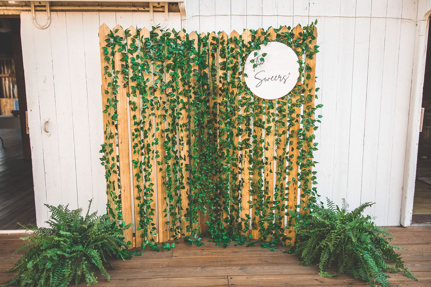 Wedding photo backdrop with cascading green vines and a round mirror against white wood paneling.