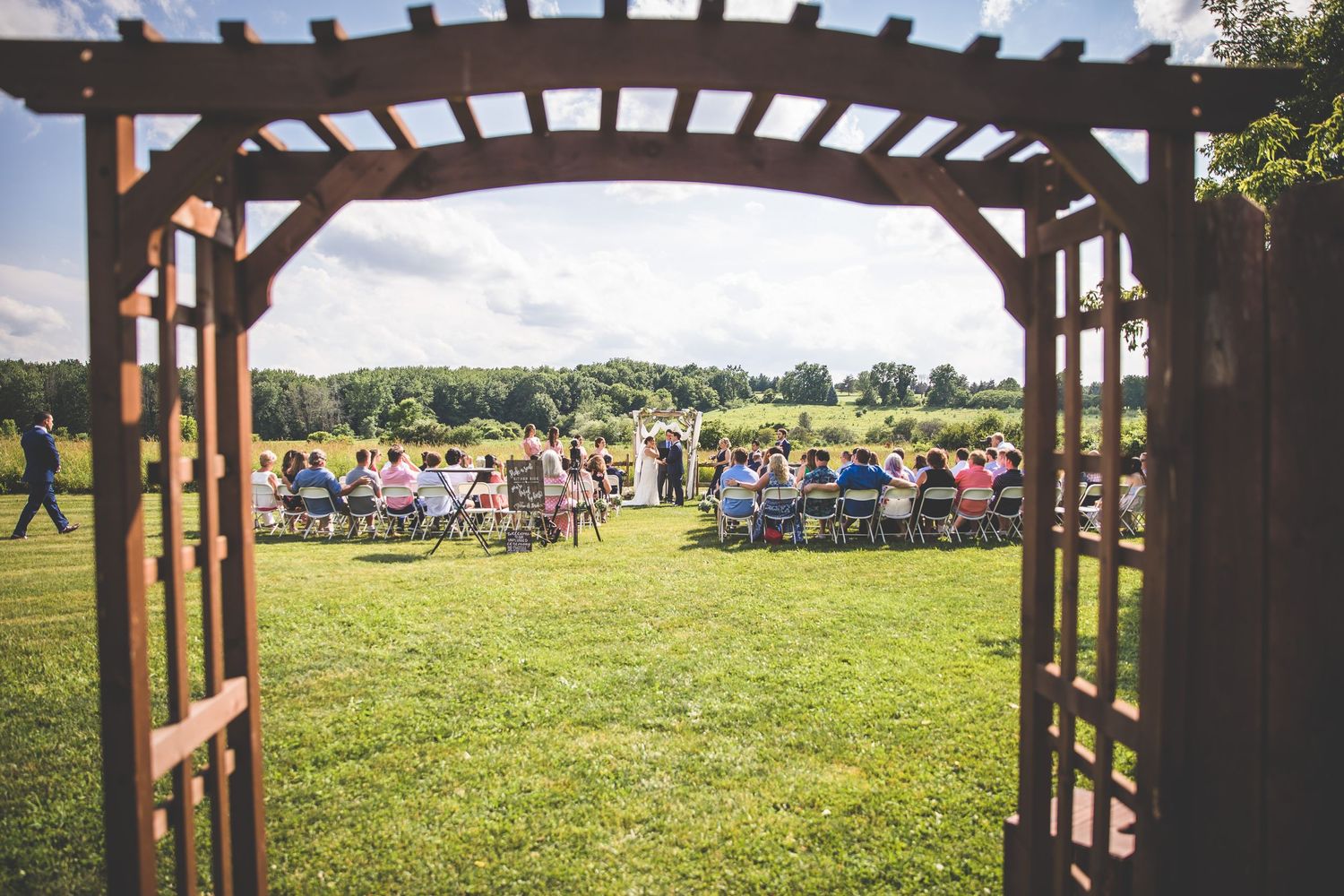 Wooden pergola arch frames a scenic outdoor wedding venue with rolling hills in the background.