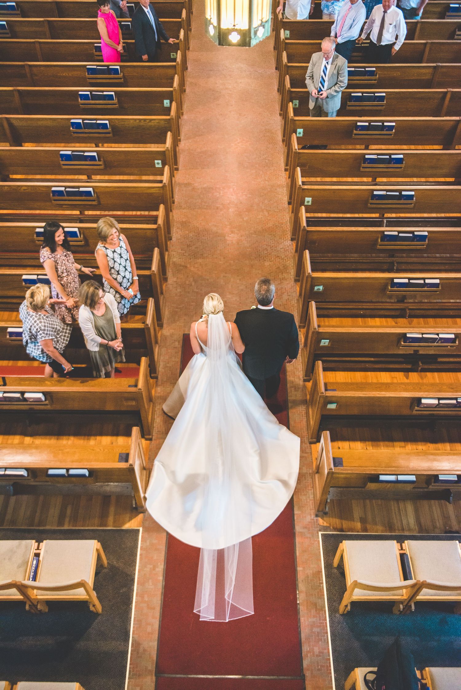 A white wedding dress flows down wooden church pews in an empty sanctuary.