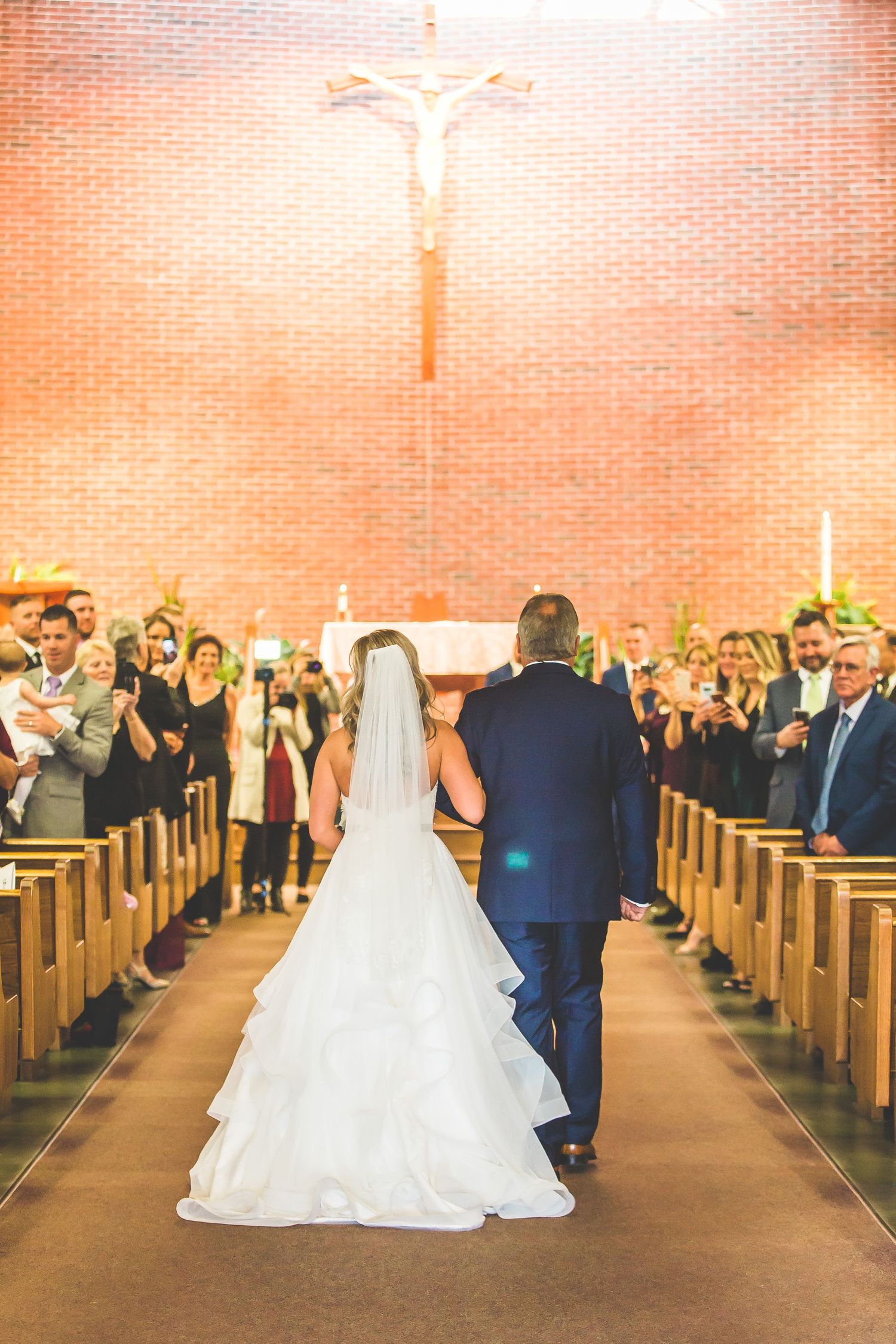 Wedding ceremony in a traditional brick church with guests standing in wooden pews.