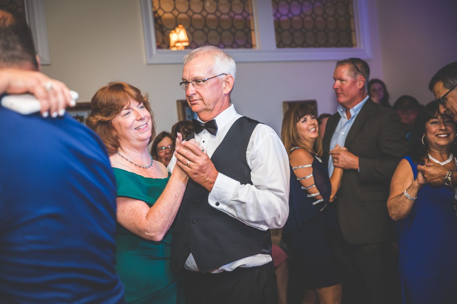 Wedding guests enjoying dancing and socializing at an indoor reception with blue accent lighting.