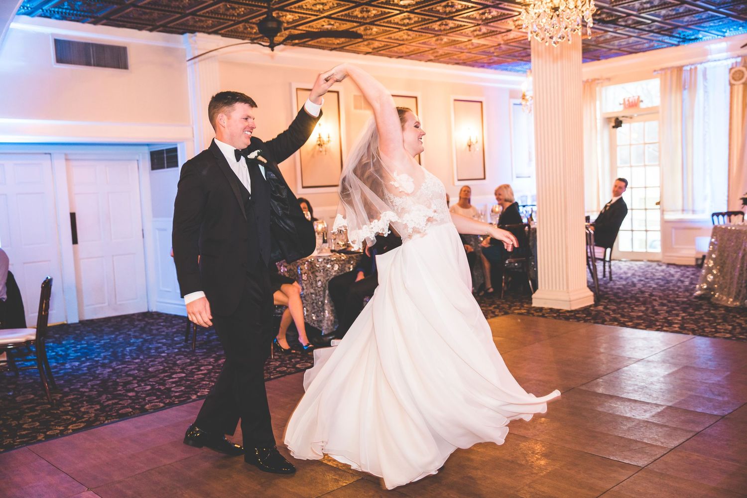 Couple sharing their first dance in a grand ballroom with dramatic lighting and chandeliers.