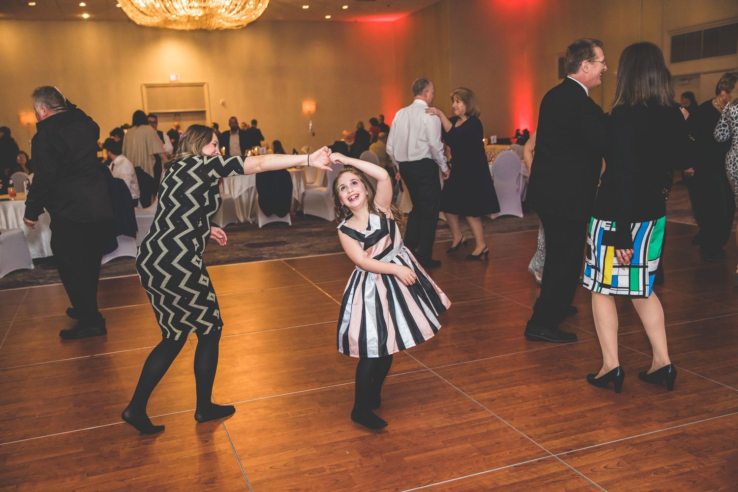 Large group of wedding guests dancing together on a wooden dance floor at reception.