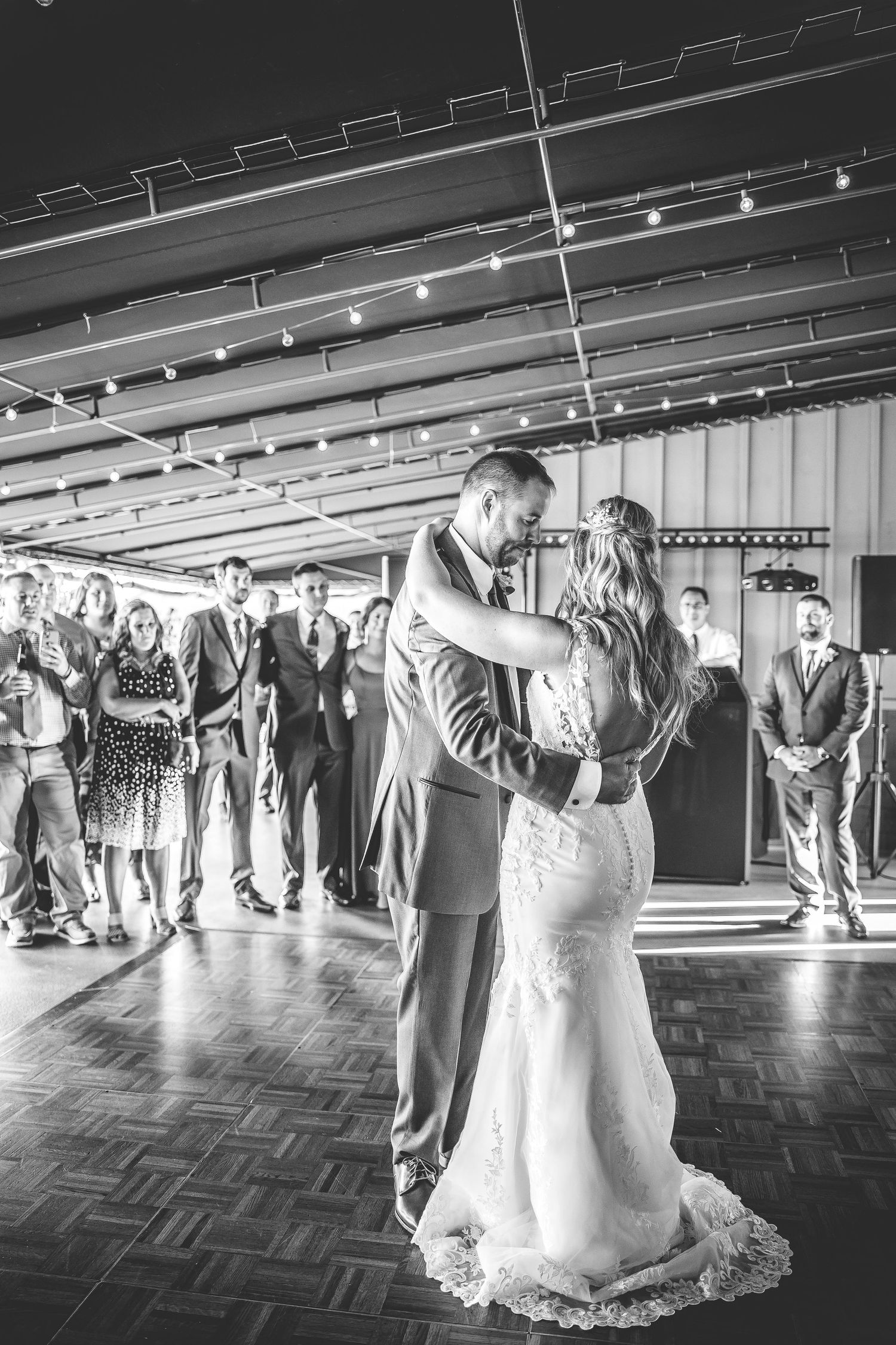 A couple performs their first dance on a parquet floor while wedding guests watch from the sides.