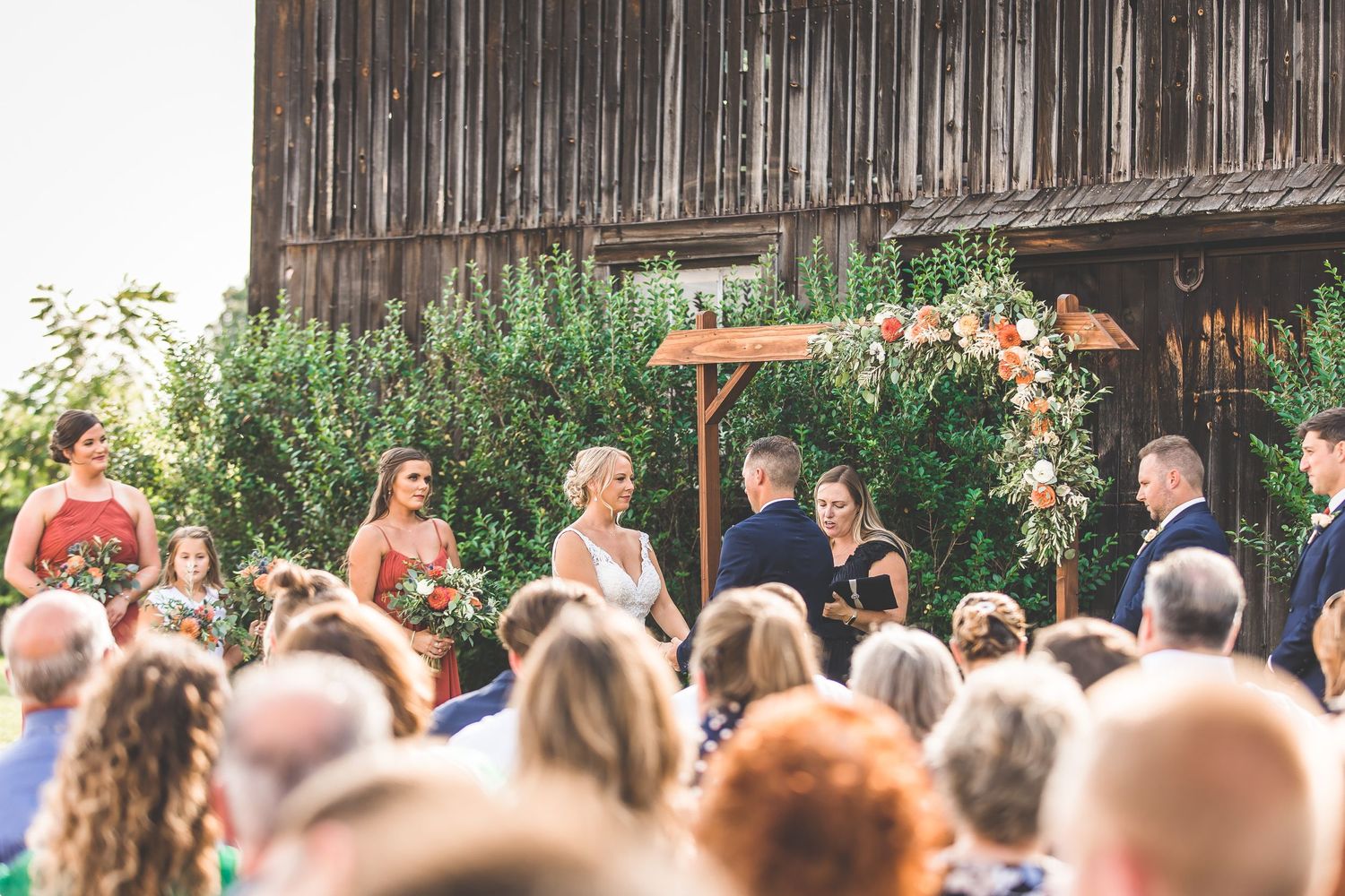 Wedding guests watching ceremony in front of rustic wooden fence backdrop.