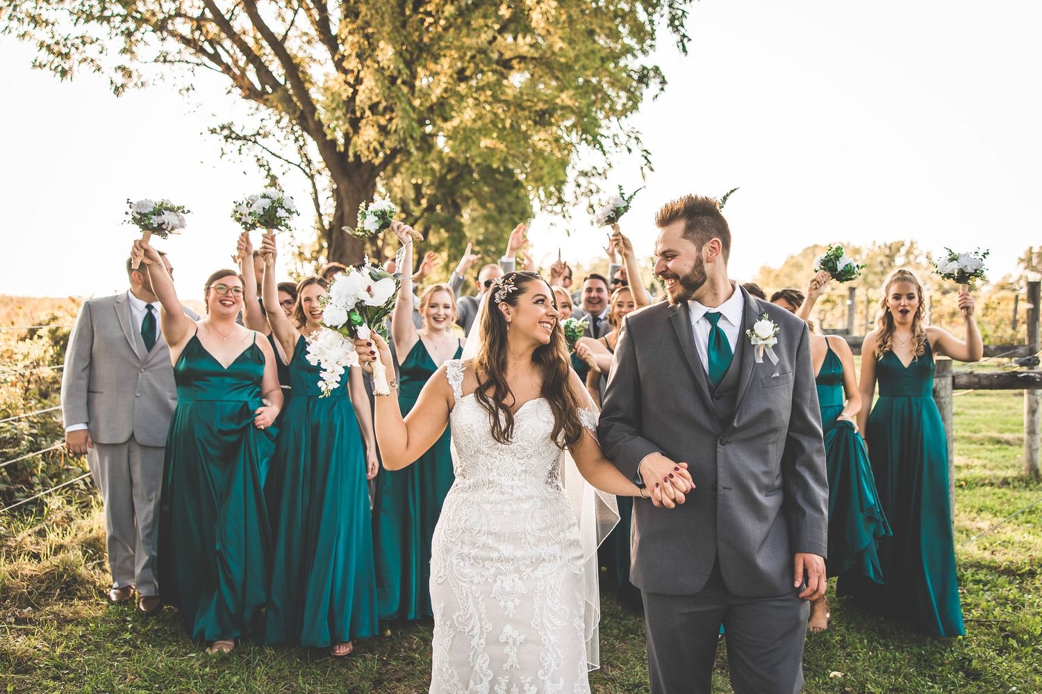Large wedding group poses together on hillside with bridesmaids in teal and groomsmen in grey.