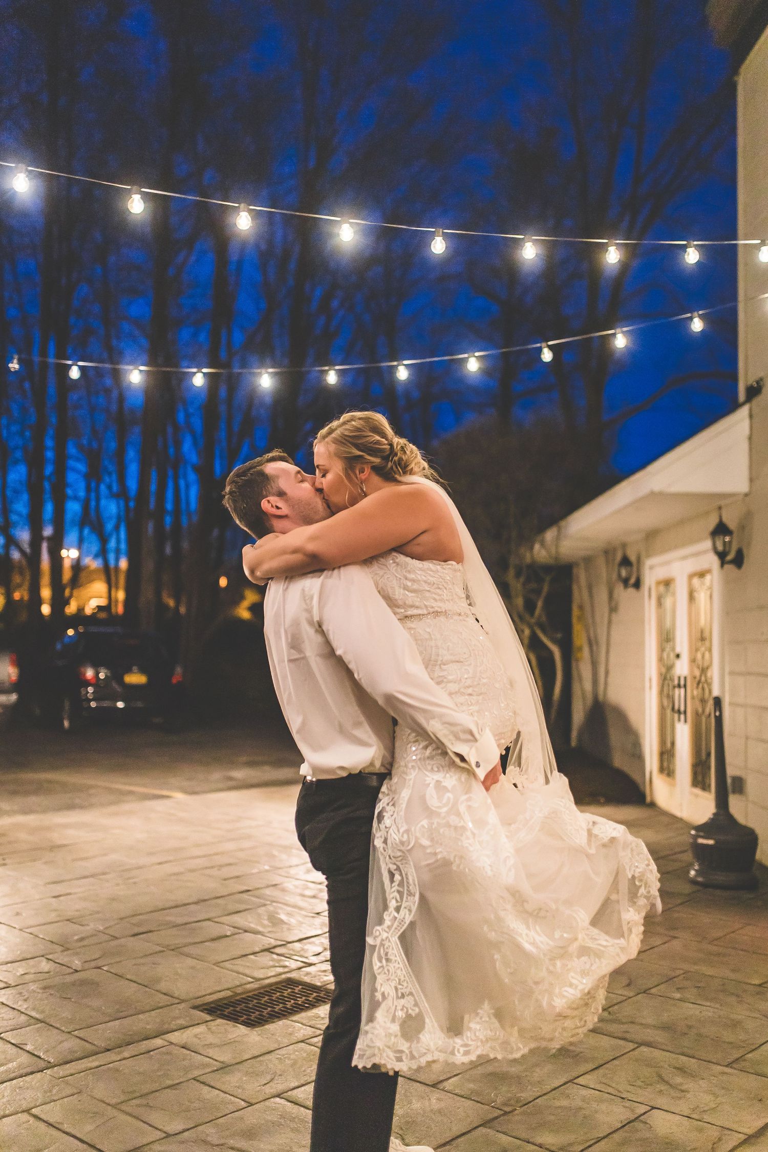 Couple dancing together under string lights on an outdoor patio at dusk.