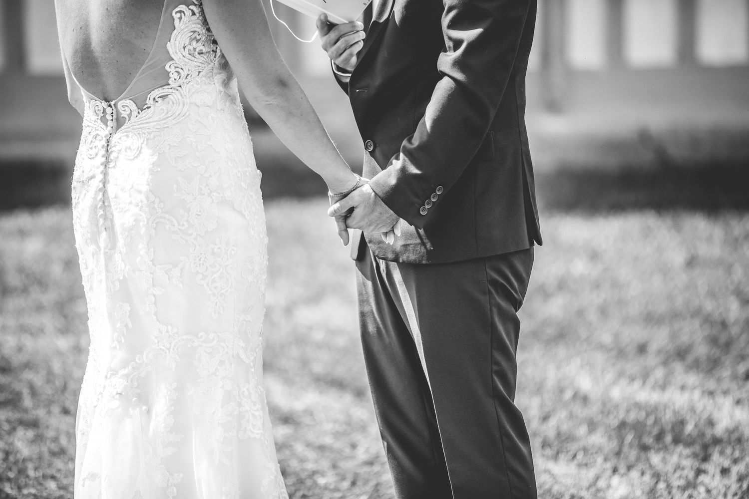 A romantic outdoor wedding scene with a couple in formal attire standing together on grassy grounds.