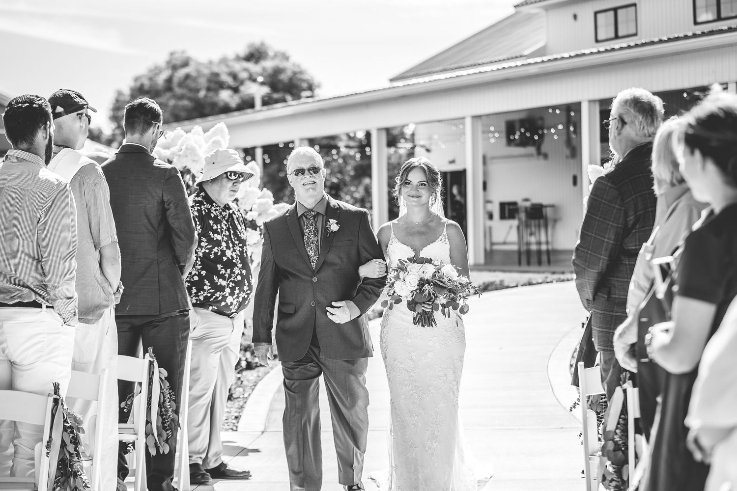 Black and white photo of outdoor wedding ceremony with guests seated on either side of aisle.