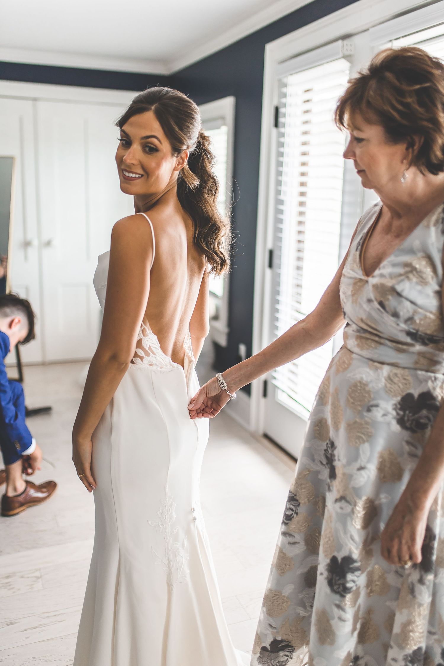 Wedding dress fitting scene with elegant white gown in a bright room with dark walls.