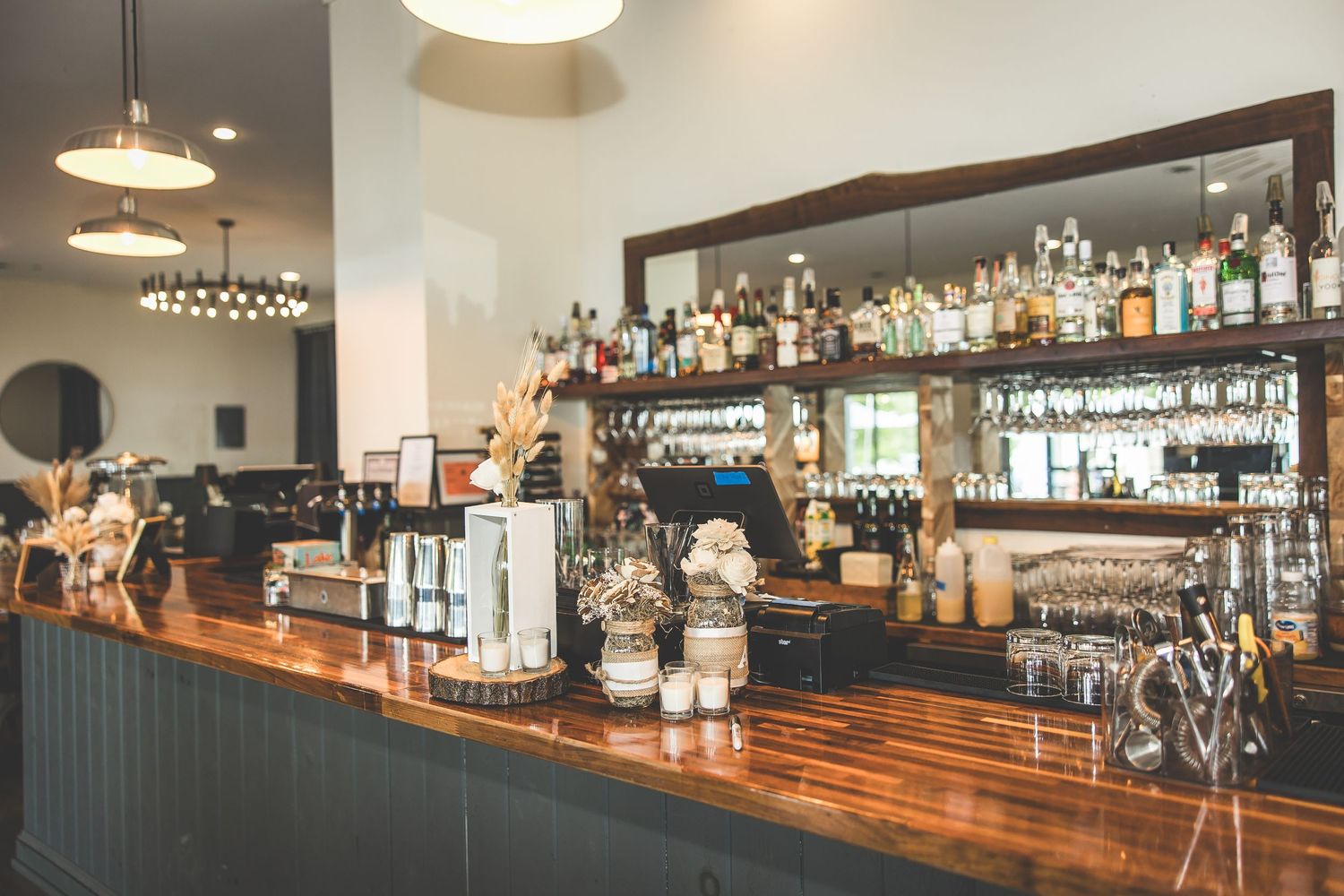 Modern bar interior with wooden countertop and shelves of liquor bottles.