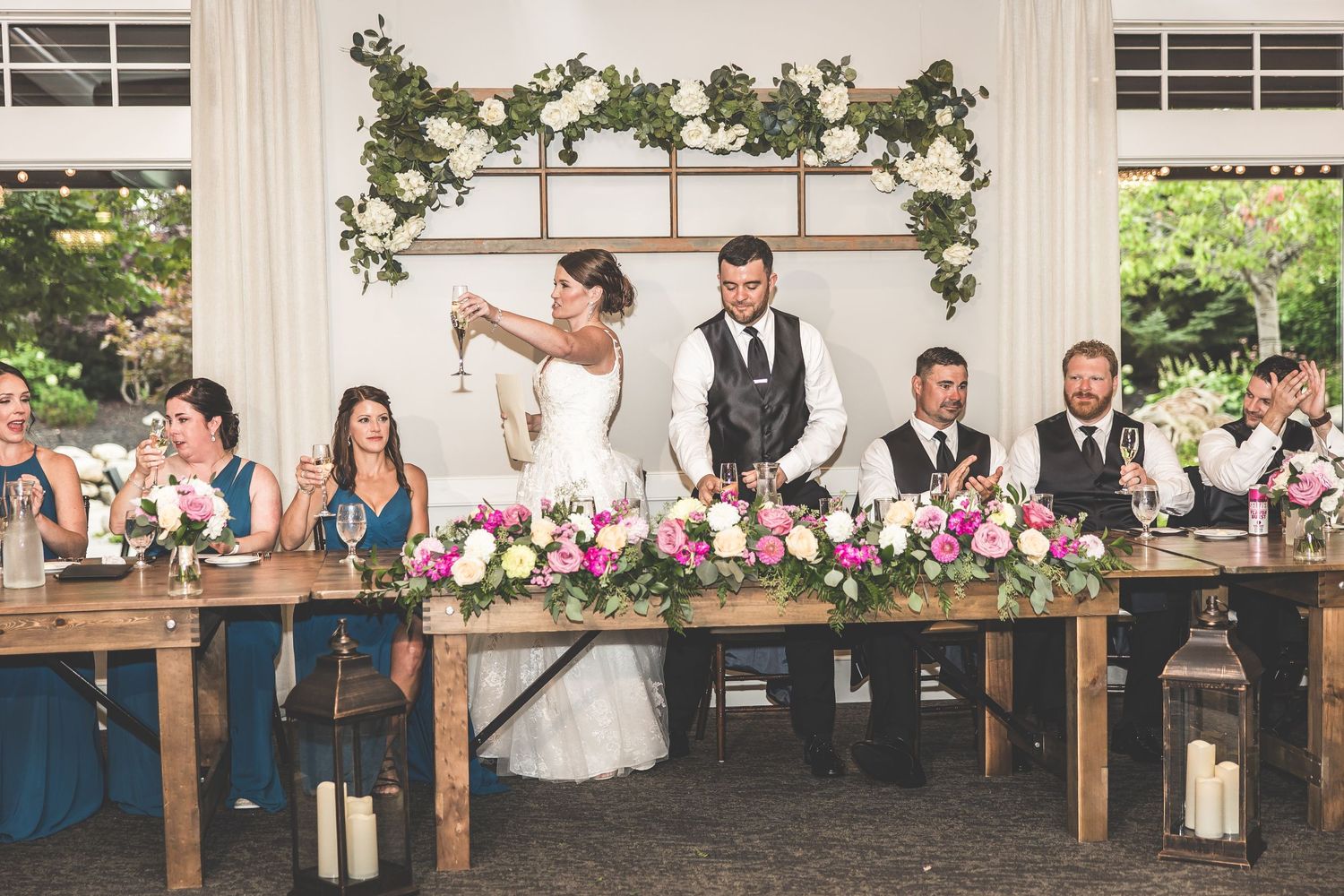 Wedding venue decorated with white drapery and pink floral arrangements on wooden tables.