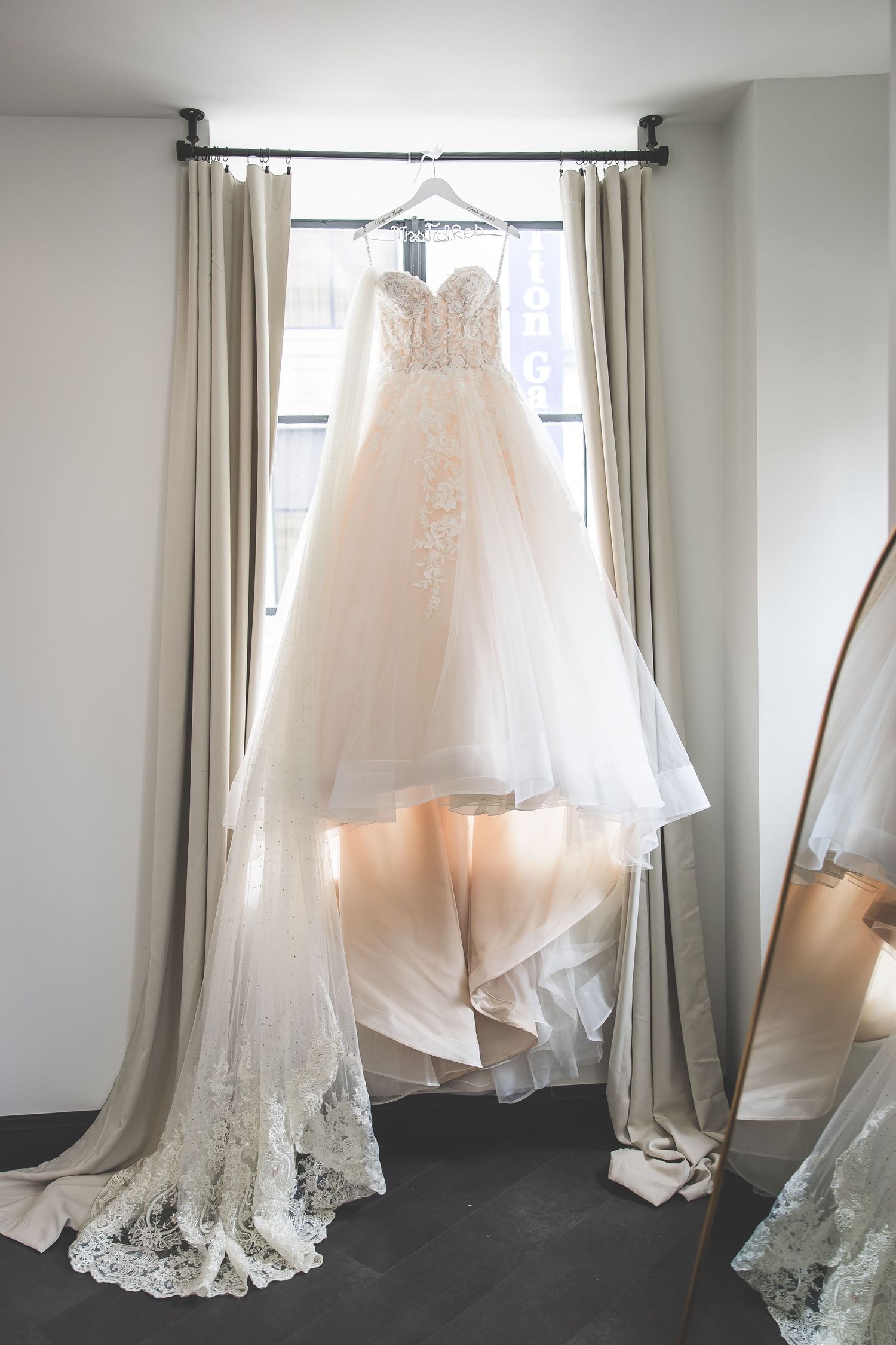 White wedding dress with lace details hanging in front of a window with natural light.