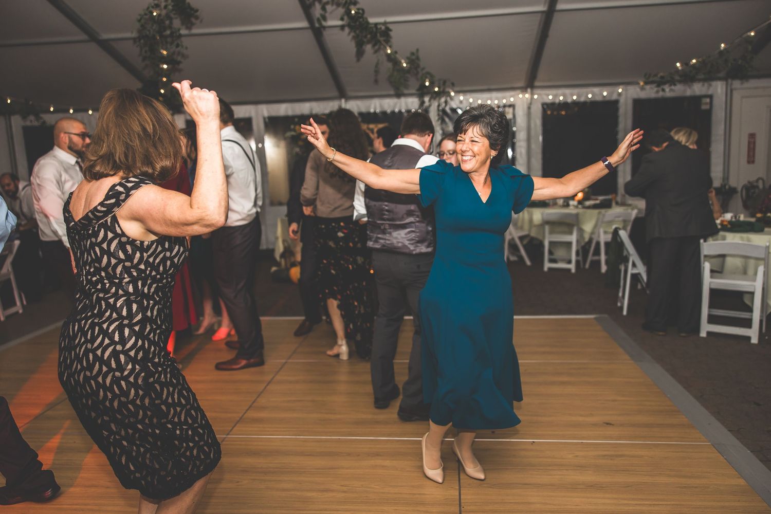Lively dance party at a wedding reception with guests moving on a wooden floor under string lights.