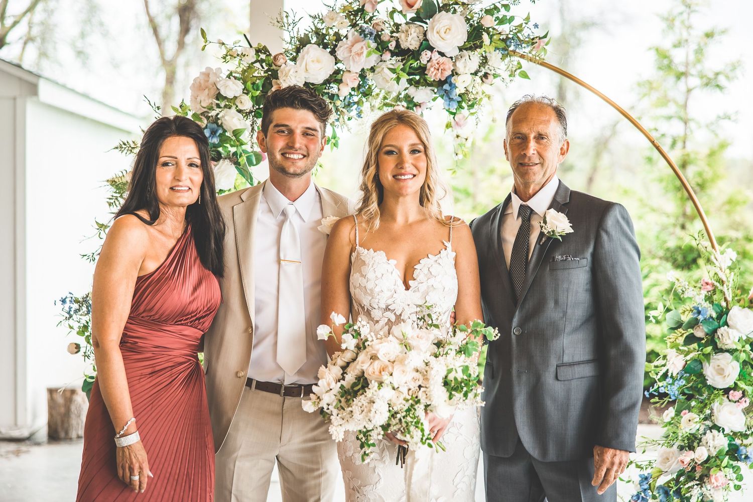 Wedding party poses under floral arch with pink and white roses.