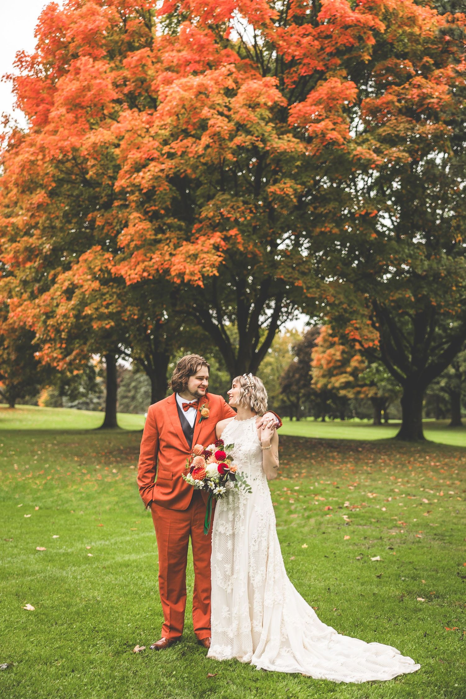 A couple celebrates their wedding day beneath magnificent orange maple trees in a park setting.